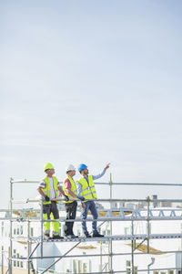 Architect showing something to colleagues while standing on scaffolding against sky