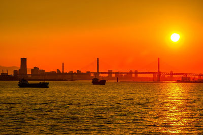 Silhouette boats in sea against orange sky