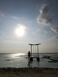 Man sitting on beach against sky during sunset