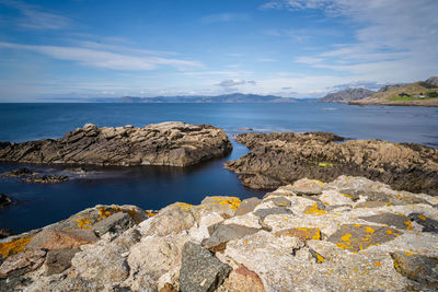 Scenic view of rocks by sea against sky