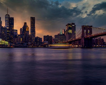 Illuminated bridge over river by buildings against sky in city