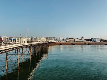 Bridge over river by buildings against clear blue sky