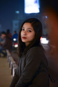 Portrait of young woman standing against illuminated lamp