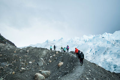 Rear view of people walking on mountain against sky