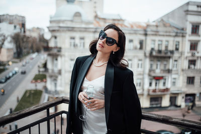 Young woman wearing sunglasses standing against railing in city