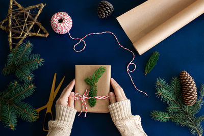 Woman wraps a handmade eco style christmas present in kraft paper and natural spruce branches 