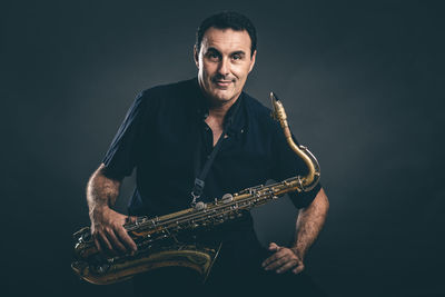 Portrait of mature man holding saxophone against black background
