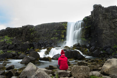 Rear view of woman sitting on rock against waterfall 