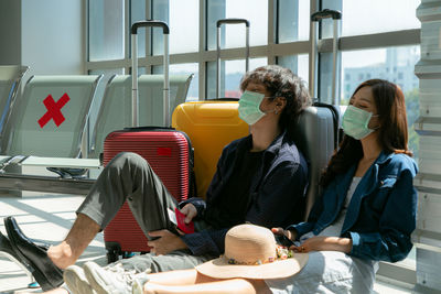 Tired female friends wearing mask sitting at airport