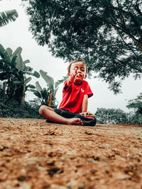 Portrait of happy girl sitting on plant against trees