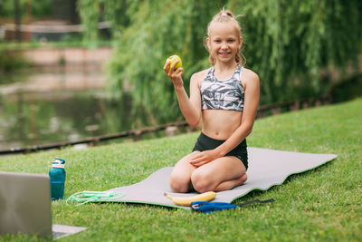 Girl with laptop eating apple on field