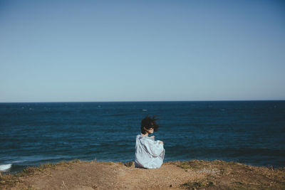 Woman sitting at beach against clear sky