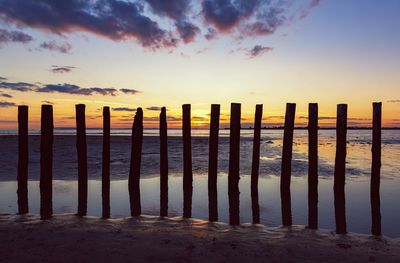 Wooden posts on beach against sky during sunset