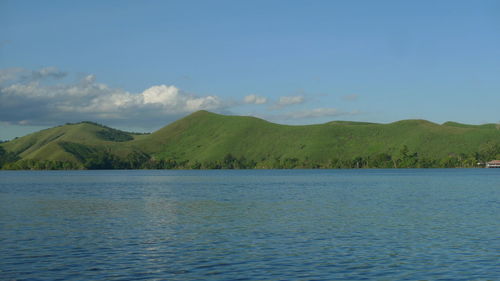 Scenic view of sea by mountain against sky