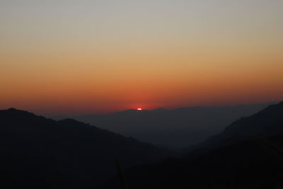 Scenic view of silhouette mountains against orange sky