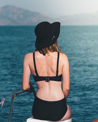 Rear view of woman sitting in bikini on seat against sea