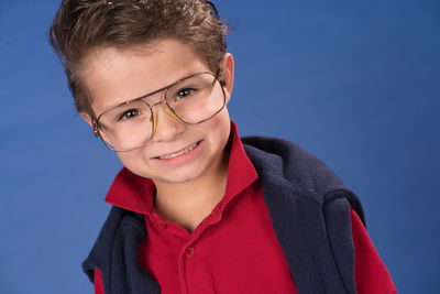 Portrait of smiling cute boy wearing eyeglasses standing against blue background