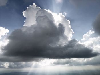 Low angle view of sunlight streaming through clouds