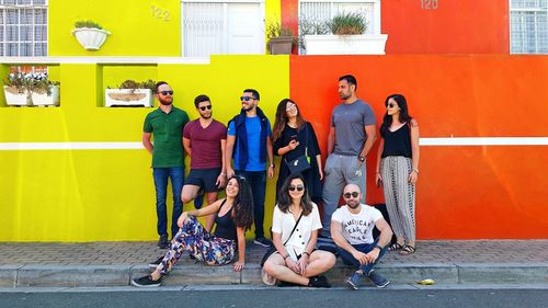 Full length of friends sitting against graffiti wall