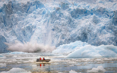 People in boat on frozen lake against glacier