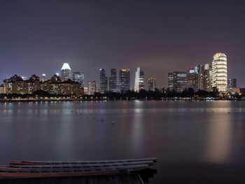 Illuminated buildings by river against sky in city at night