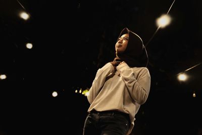 Low angle view of young woman standing under illuminated ceiling