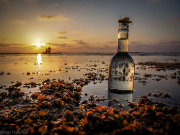 Water filled bottle at beach during sunset