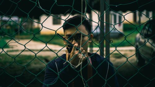 Portrait of man talking on walkie-talkie seen through chainlink fence