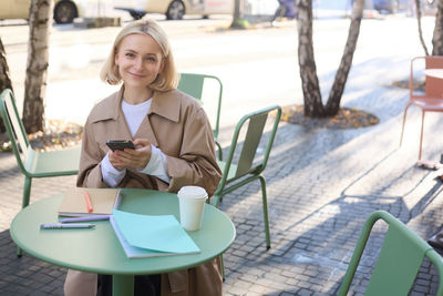 Portrait of young woman using mobile phone while sitting on table