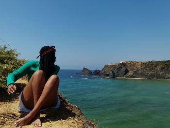 Full length of woman sitting by sea against sky