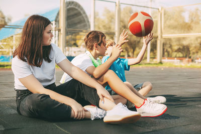 Cheerful high school students sit on the basketball court, relax after the game, talk and laugh.