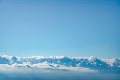 A desktop wallpaper background of blue skies with fluffy clouds filling the lower half of the image