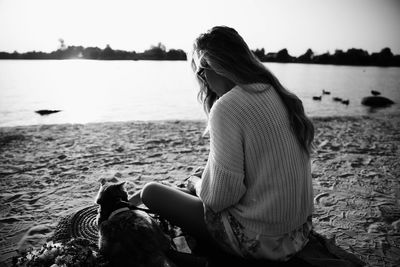 Woman sitting on beach by sea against sky