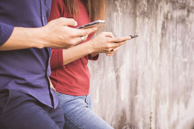 Midsection of man and woman using mobile phones against wall