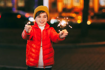 A charming boy holds a sparkler in his hands, celebrating the new year at night on the street. 