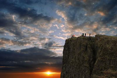 Low angle view of rocks on cliff against sky during sunset