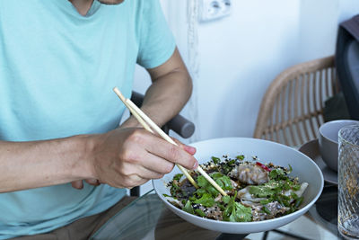 Man eating chopsticks healthy vegan food jiaozi with tofu and vegetables in soy sauce chinese dish