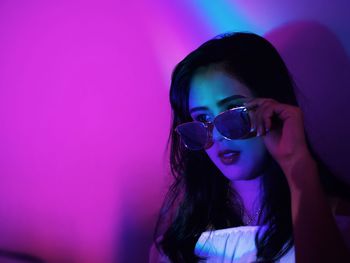 Young woman wearing sunglasses while looking away in illuminated room