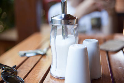 Close-up of salt shaker with empty drinking glasses by sunglasses on table
