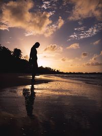 Silhouette woman standing at beach against sky during sunset