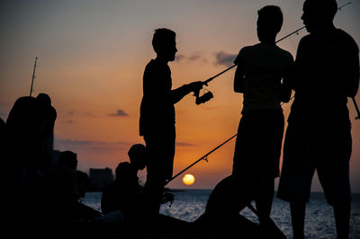 Silhouette people fishing by sea during sunset