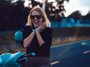 Portrait of cheerful young woman wearing sunglasses sitting on motor scooter