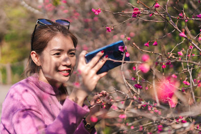 Smiling woman photographing pink flowers with mobile phone