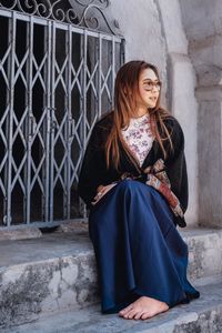 Young woman with long brown hair sitting on steps at entrance of building