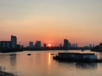 Buildings by river against sky during sunset
