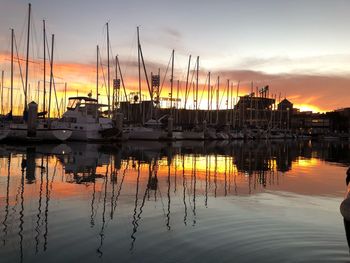 Sailboats moored at harbor against sky during sunset