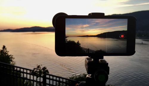 Close-up of camera on sea against sky during sunset