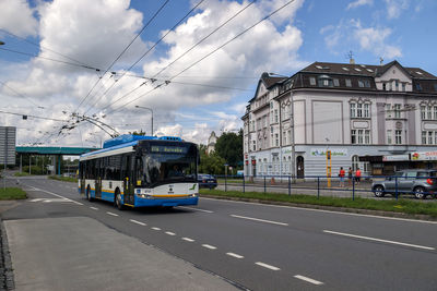 Vehicles on road by buildings in city against sky