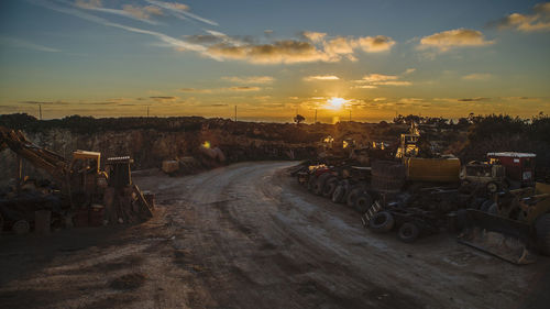 Road amidst junkyard against sky during sunset