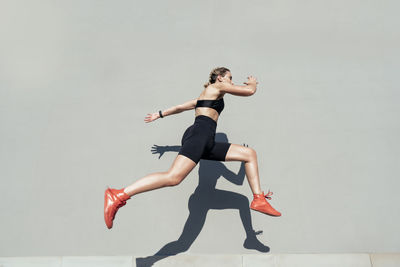 Young athlete jumping by gray wall on sunny day